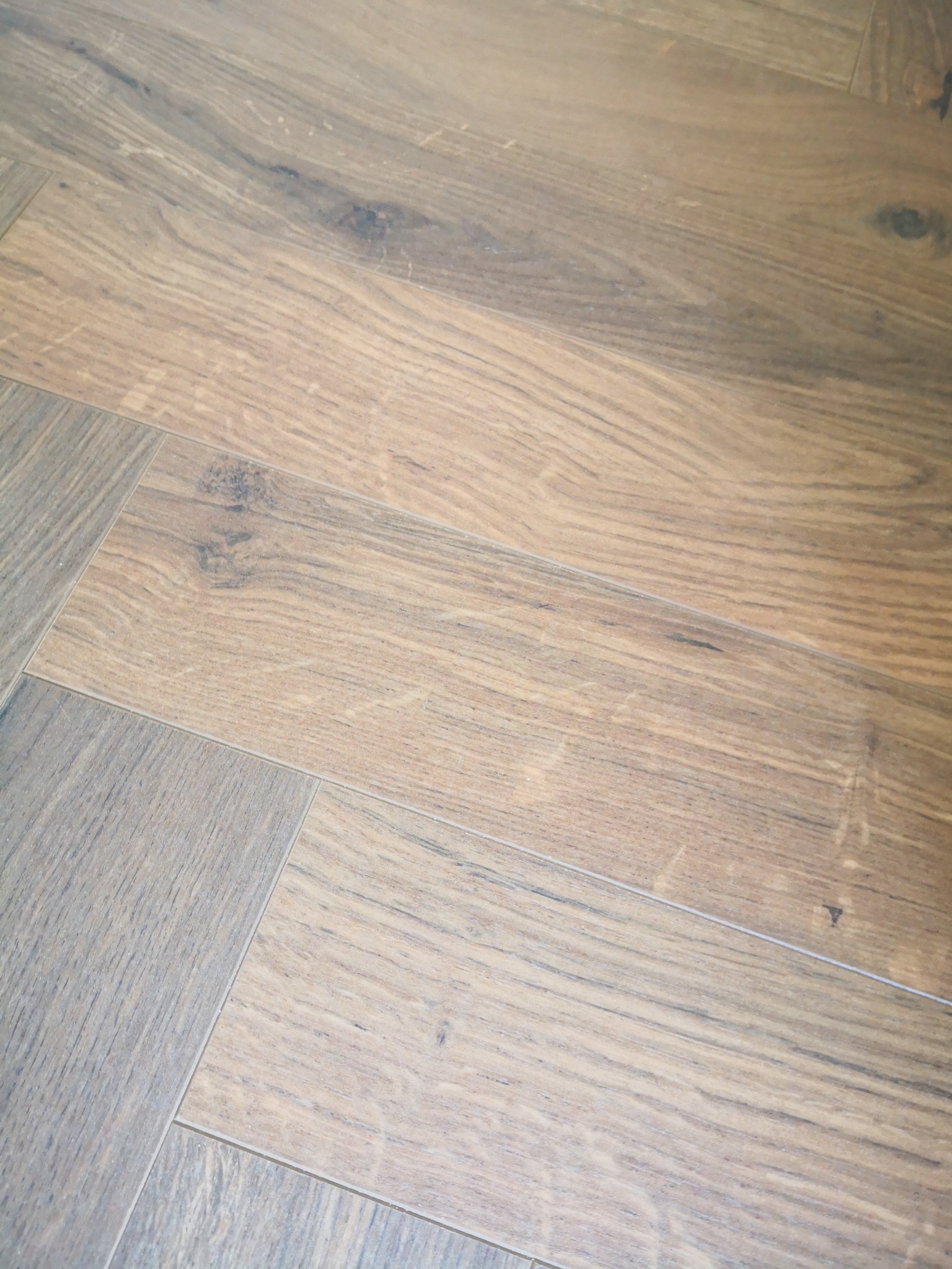 Ułożona podłoga z desek w odcieniach naturalnego drewna i szarości, widoczne delikatne słoje i łączenia, ułożone w sposób imitujący parkiet.