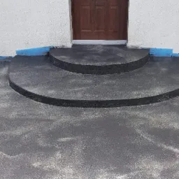 Schody wejściowe wykończone ciemnym mikrocementem, z widocznym zabezpieczeniem folią na styku z trawnikiem.