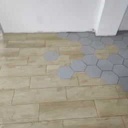 Układanie jasnych płytek imitujących drewno i szarych heksagonalnych płytek na podłodze w trakcie remontu.