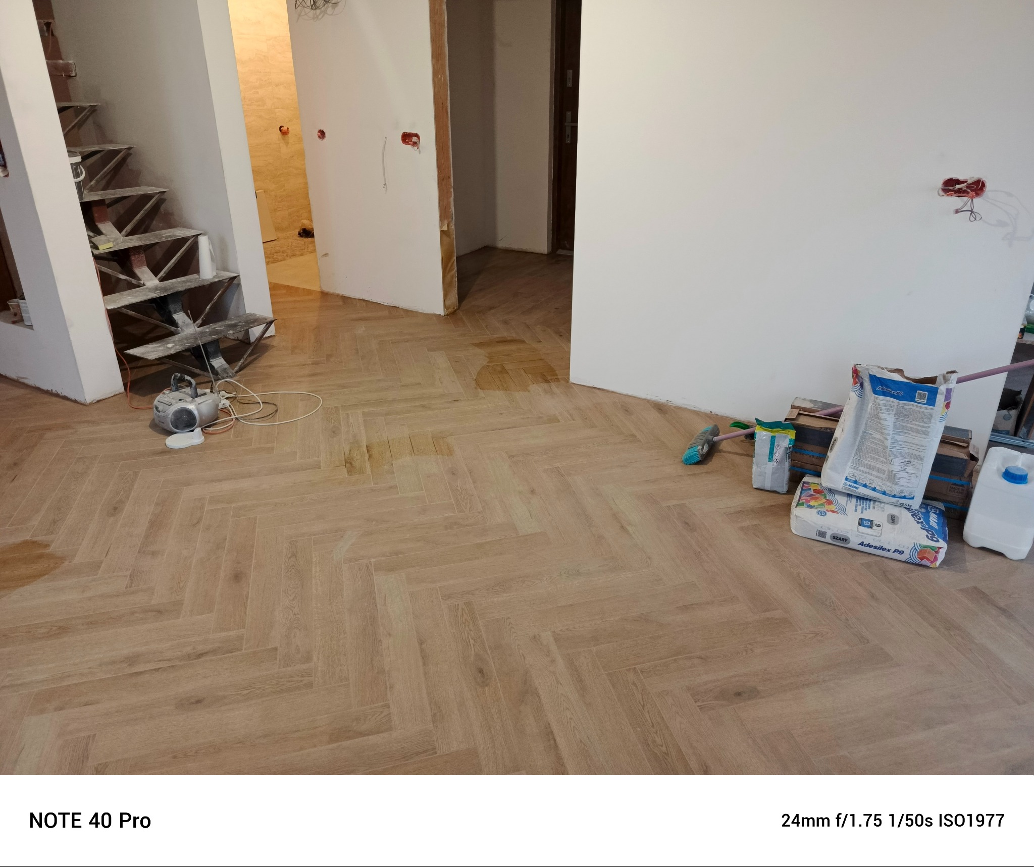 Ułożona podłoga z paneli w jodełkę w trakcie prac wykończeniowych w Siemianowicach Śląskich, widoczne worki z klejem, drabina i narzędzia.