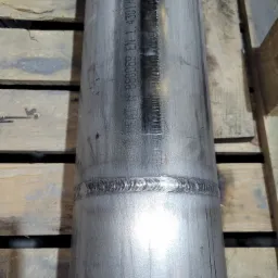 Połączenie spawane na rurze ze stali nierdzewnej, widoczne oznaczenia normy EN 1.4301/EN 1.5307 na powierzchni, ułożona na drewnianej palecie.