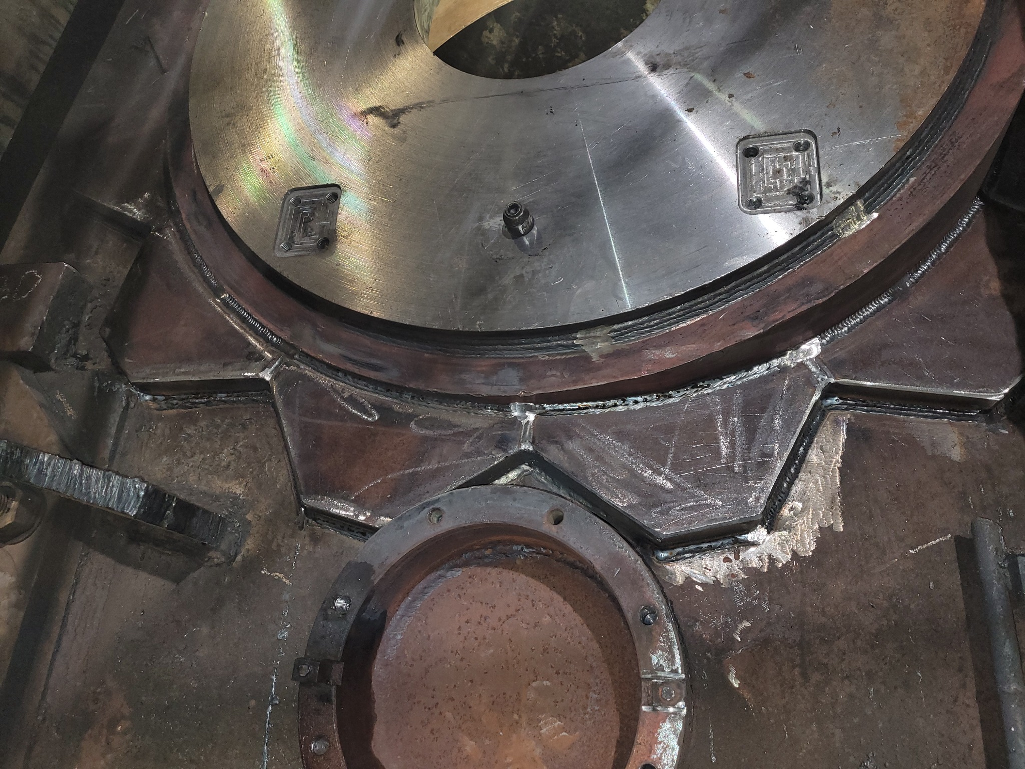 Detale spawanych elementów konstrukcji stalowej z widocznymi śladami obróbki i spawania, z okrągłym otworem w dolnej części.