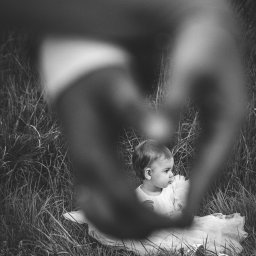 mgartfoto - Czarno-białe zdjęcie dziewczynki w białej sukience siedzącej w trawie, uchwyconej przez dłonie tworzące kształt serca w Końskich.