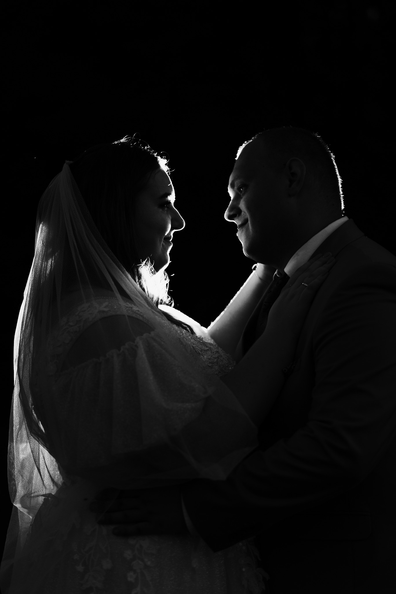 Czarno-białe zdjęcie sylwetek pary młodej wpatrzonych w siebie, z delikatnym podświetleniem konturów i ciemnym tłem.