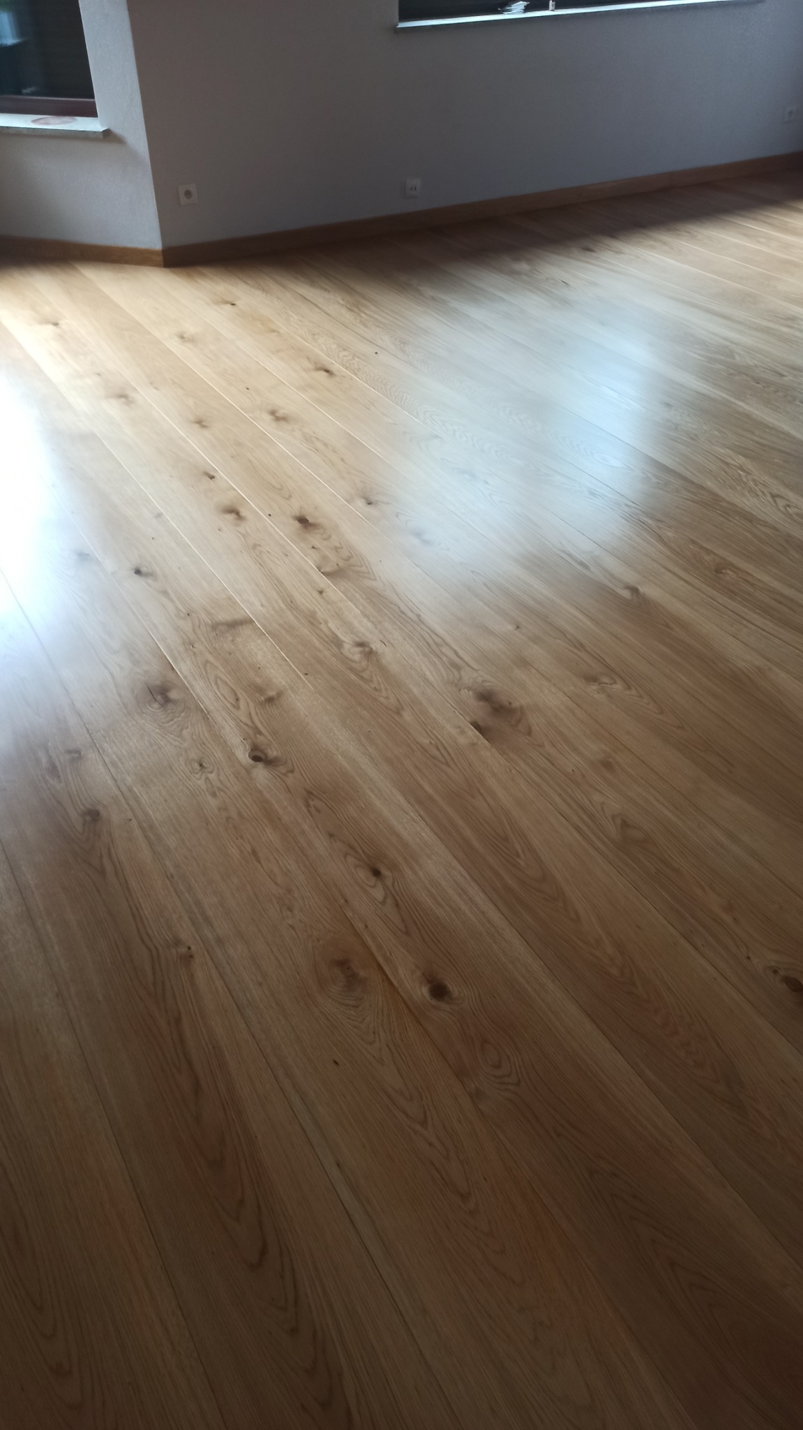 Jasny parkiet ułożony w nowym pomieszczeniu, widoczne gniazdka elektryczne przy podłodze, delikatne odbicie światła na powierzchni.