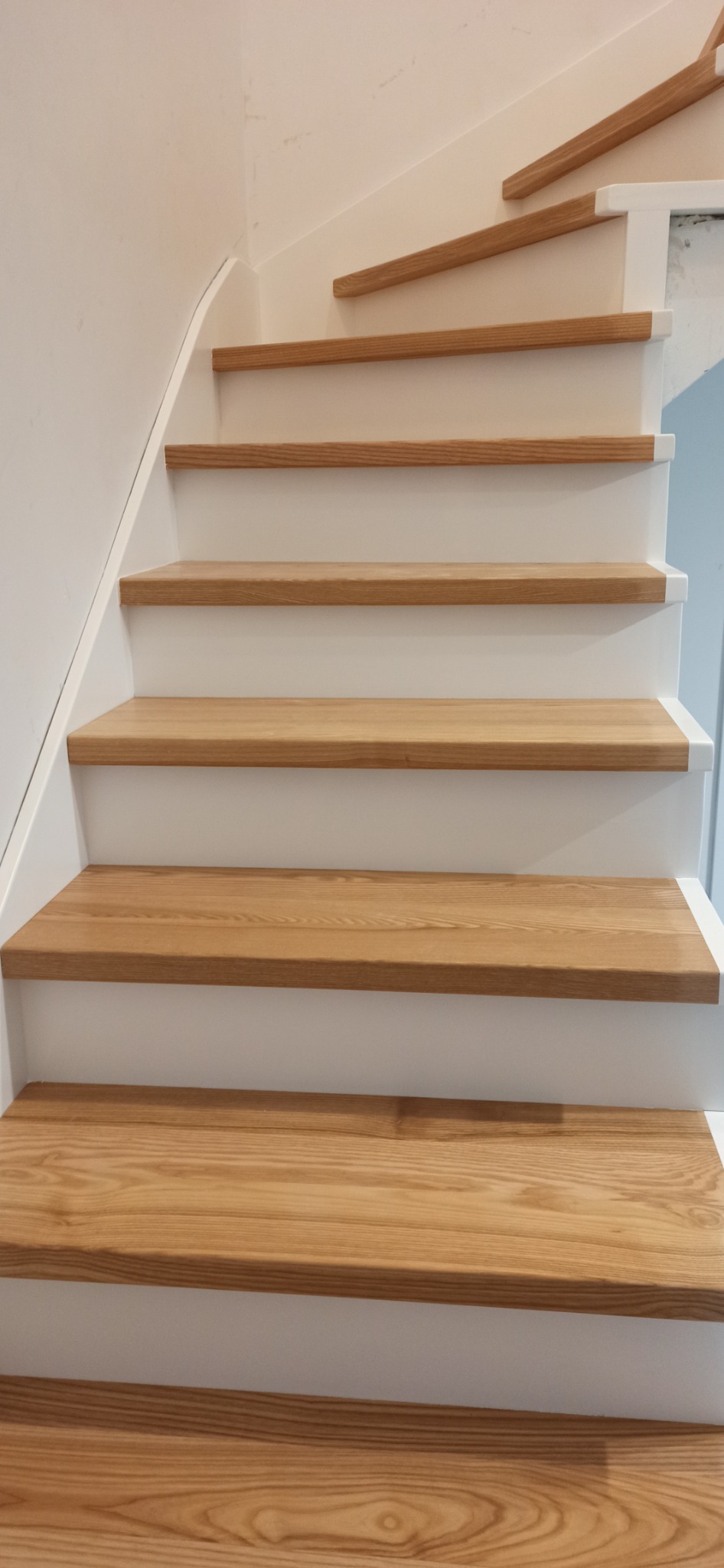 Jasne drewniane schody z białymi podstopnicami, widok z dołu, naturalne oświetlenie eksponuje usłojenie drewna.