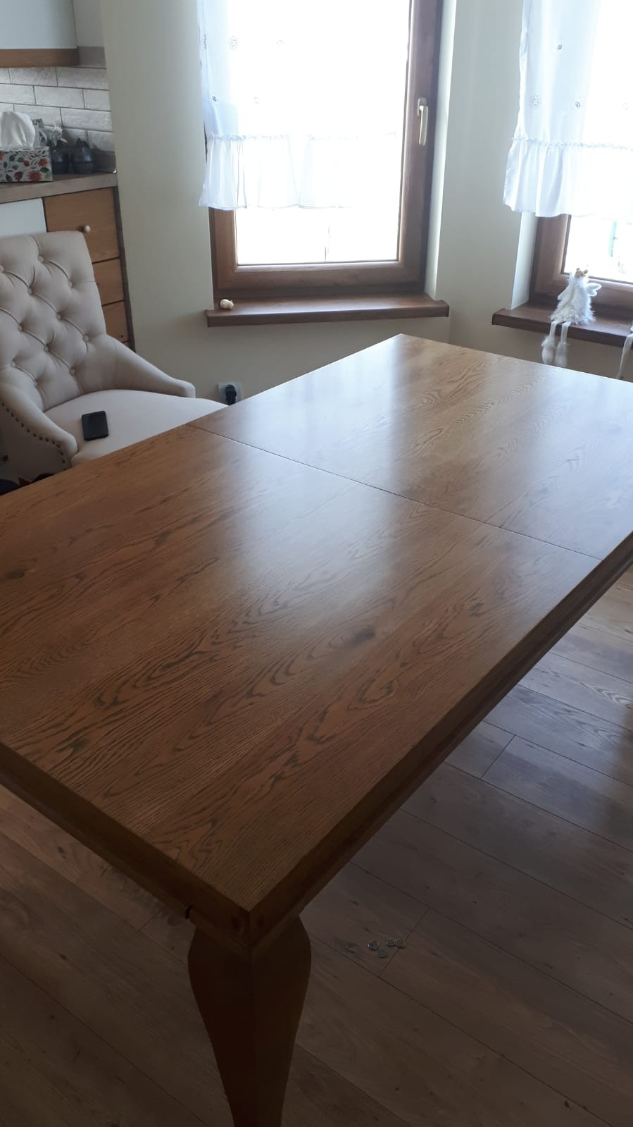 Rozkładany stół z drewna o ciepłym odcieniu, z widocznym usłojeniem, ustawiony w jasnym wnętrzu z drewnianą podłogą i krzesłem w stylu vintage w tle.