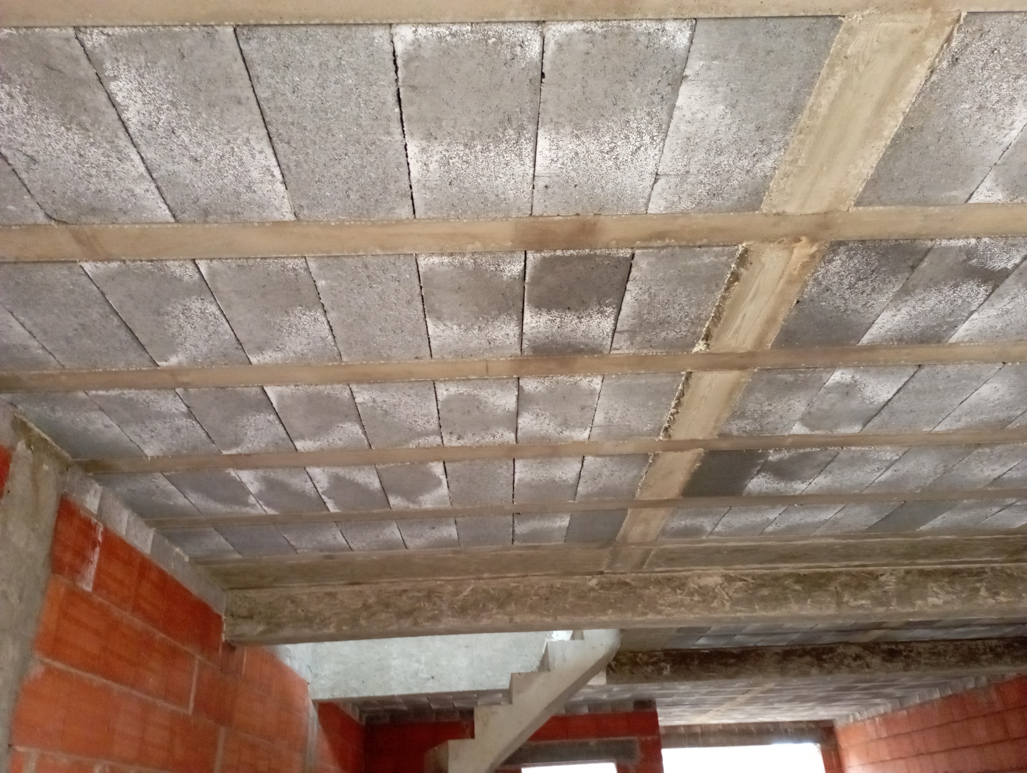Wnętrze w trakcie budowy: widok na strop z szarego pustaka ceramicznego, wzmocniony żebrami, ściany z czerwonej cegły, fragment schodów.