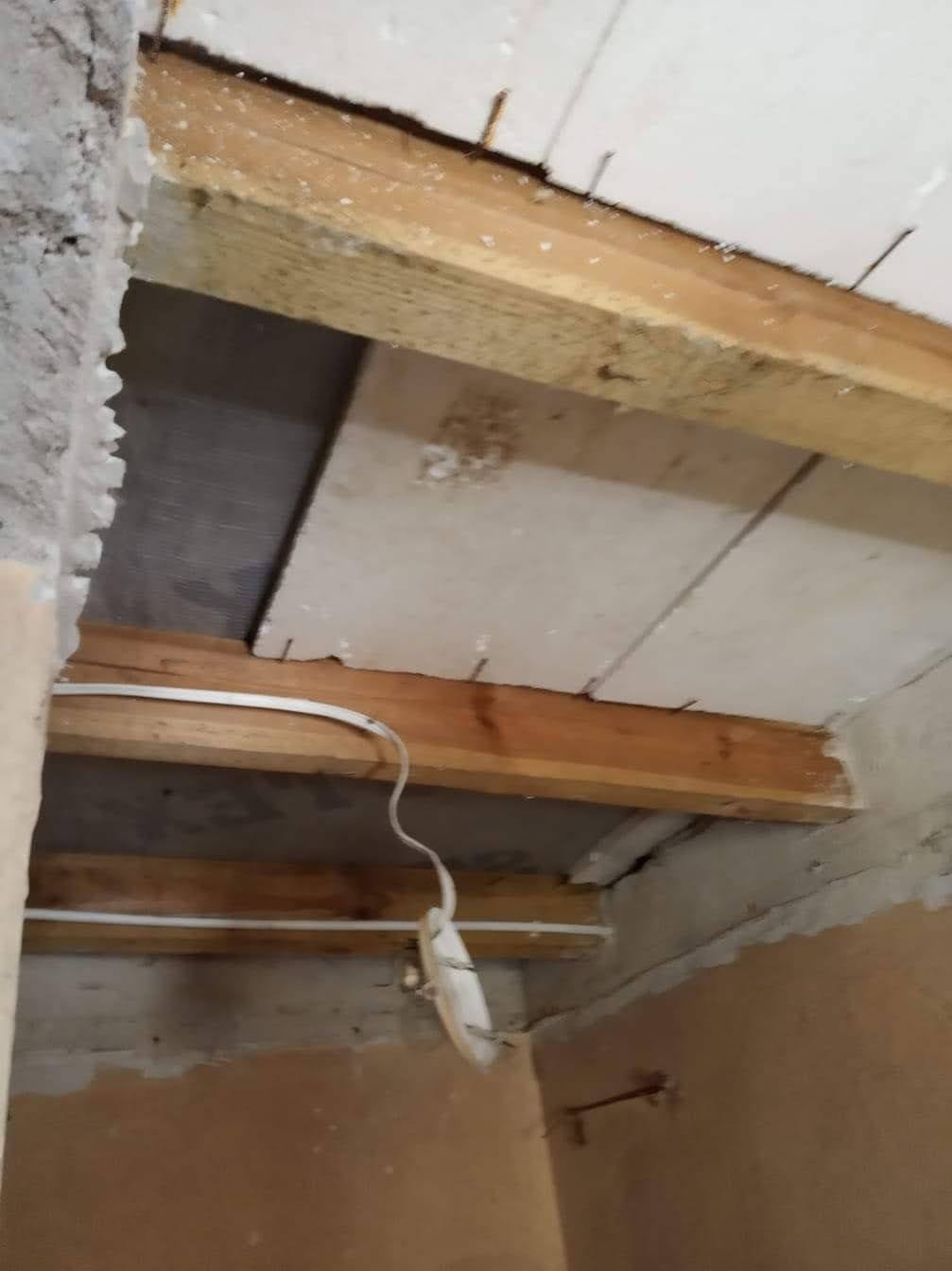 Poddasze w trakcie ocieplania z widocznymi drewnianymi belkami, przewodami elektrycznymi i fragmentami izolacji.