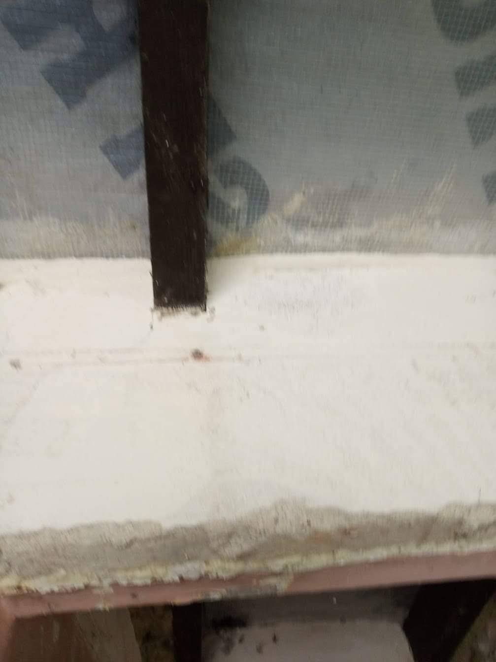 Fragment ściany z nałożoną warstwą gładzi, widoczna siatka wzmacniająca i pionowa listwa. Surowy stan wykończenia, zbliżenie na detale.