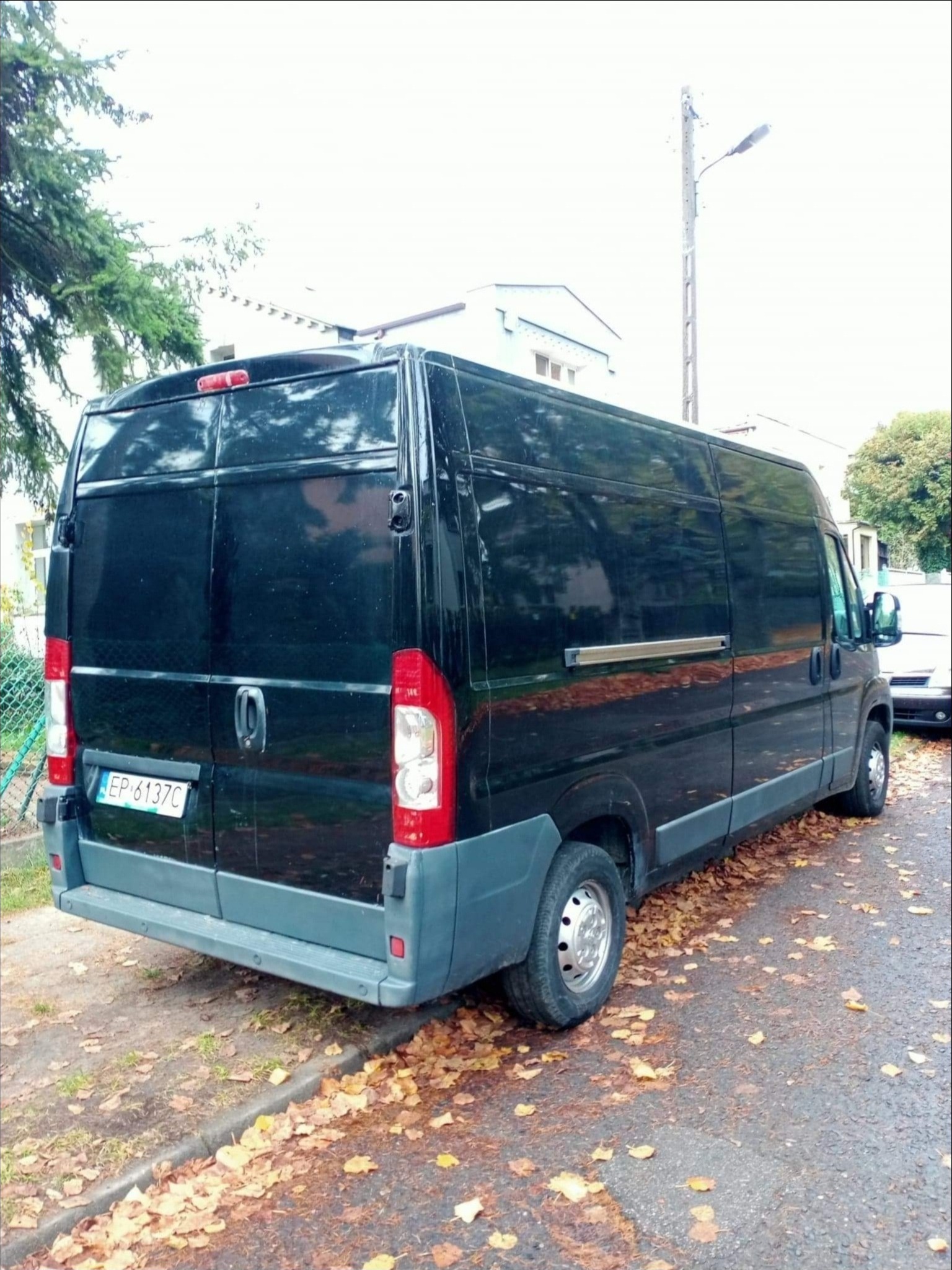 Czarny bus dostawczy zaparkowany na ulicy z opadłymi liśćmi, widok z tyłu, tablica rejestracyjna EP 6137C widoczna.