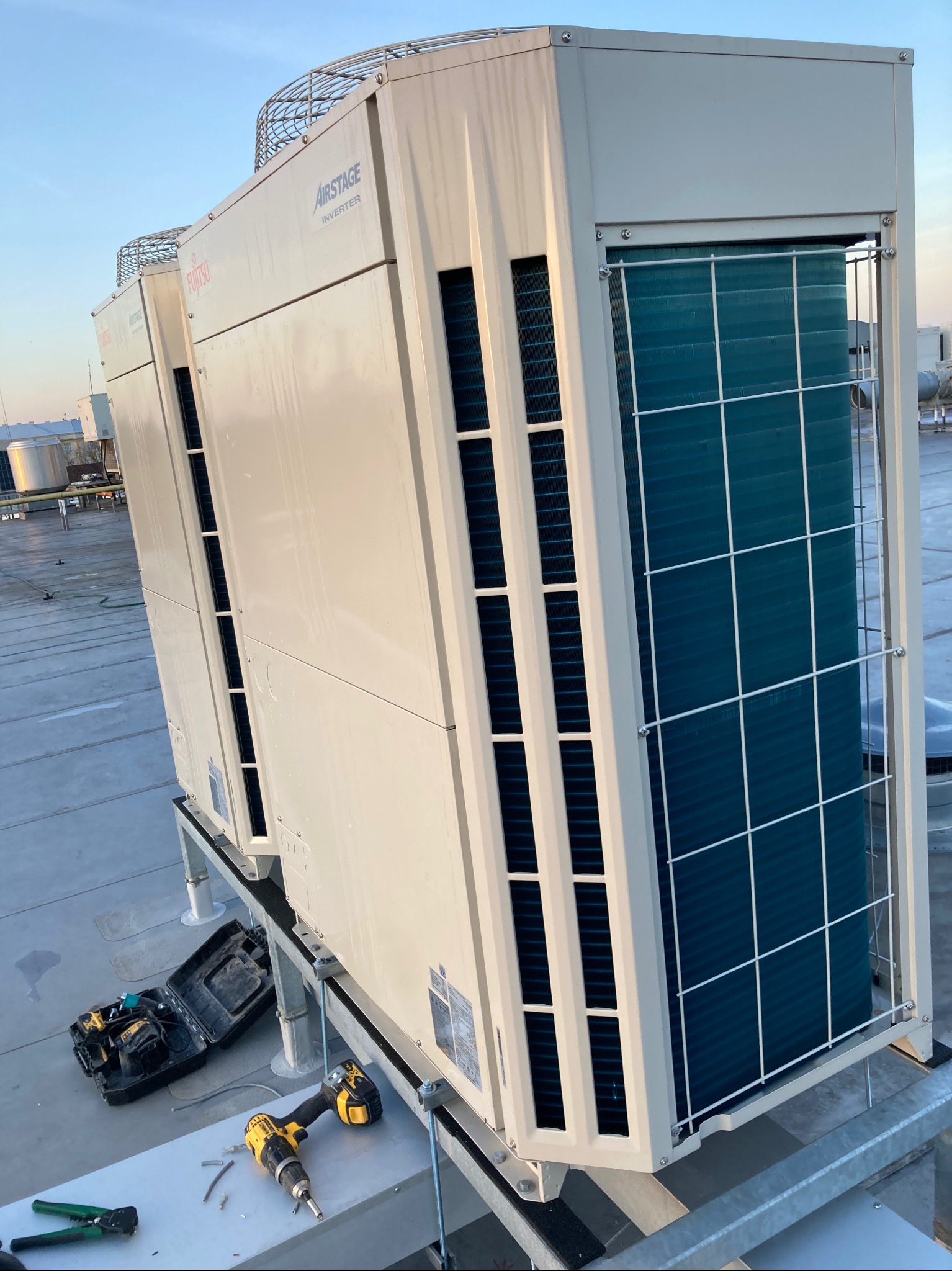 Dwa agregaty klimatyzacyjne Fujitsu Airstage Inverter na dachu budynku komercyjnego, widoczne narzędzia i skrzynka narzędziowa sugerują montaż lub serwis.