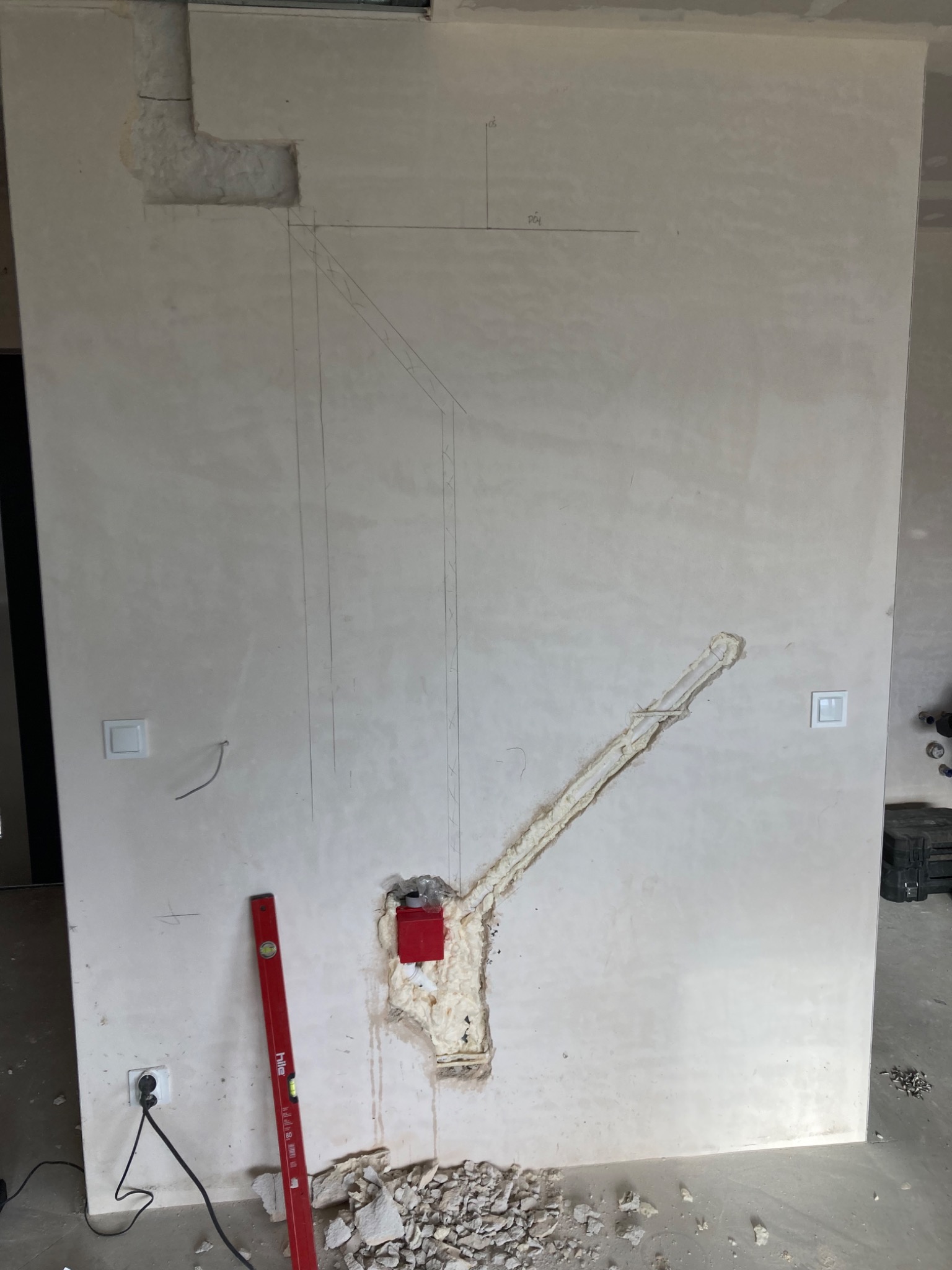 Ściana w trakcie montażu instalacji wentylacyjnej z zaznaczonym przebiegiem kanałów, widoczne otwory wypełnione pianką montażową, poziomica i kabel zasilający