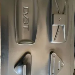 Srebrna forma wtryskowa z czterema różnymi kształtami, w tym jeden z napisem 'DVBT', ukazana z góry.