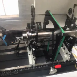 Wyważarka firmy Schenck z zamontowanym elementem metalowym, widoczne czujniki, paski napędowe i skala pomiarowa.