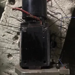 Czarno-srebrna głowica tokarska z przewodami na tle betonowej ściany z widocznymi śladami obróbki.