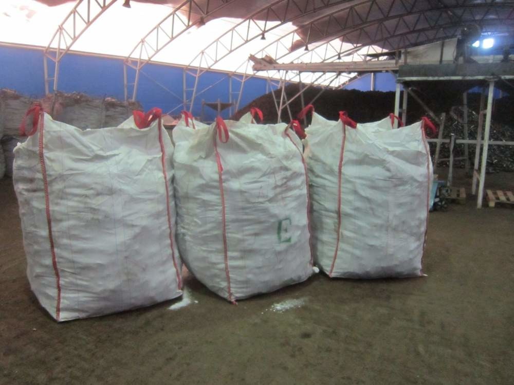 Trzy białe worki typu big bag z czerwonymi uchwytami, prawdopodobnie wypełnione agropelletem lub brykietem, stoją na betonowej podłodze w hali magazynowej z widocznymi konstrukcjami stalowymi...