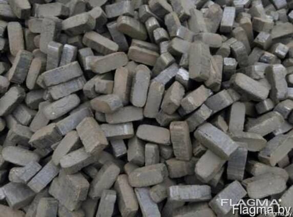 Stos szarych, prostokątnych brykietów węglowych ułożonych chaotycznie, widoczne nierówności i pęknięcia na powierzchni materiału.