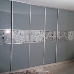 Szafa przesuwna z szarymi frontami i dekoracyjnym pasem z wzorem abstrakcyjnych liści, widoczna z perspektywy pokoju.