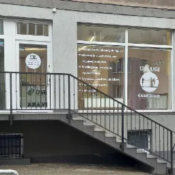 Wejście do zakładu krawieckiego z widocznymi schodami, balustradą, drzwiami z naklejką informacyjną o godzinach otwarcia oraz oknem z listą oferowanych usług, takich jak dopasowywanie odzieży...