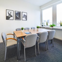 Kancelaria Gospodarcza EFFEKTI sp. z o.o. - Jasna sala konferencyjna z drewnianym stołem, szarymi krzesłami, trzema obrazami zwierząt na ścianie i roślinami w doniczkach na parapecie okiennym z widokiem na miasto.