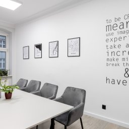 Kancelaria Gospodarcza EFFEKTI sp. z o.o. - Jasne, minimalistyczne biuro w Poznaniu z białym stołem konferencyjnym, szarymi krzesłami, roślinami doniczkowymi i ścianą ozdobioną mapami miast oraz inspirującym napisem 'to be CREATIVE means...'.
