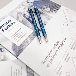 Kancelaria Gospodarcza EFFEKTI sp. z o.o. - Dwa niebieskie długopisy z logo firmy Partner Gospodarczy leżą na materiałach reklamowych Grupy Farkas oferującej kompleks usług w jednym miejscu, w tym rejestrację i sprzedaż spółek oraz biuro...