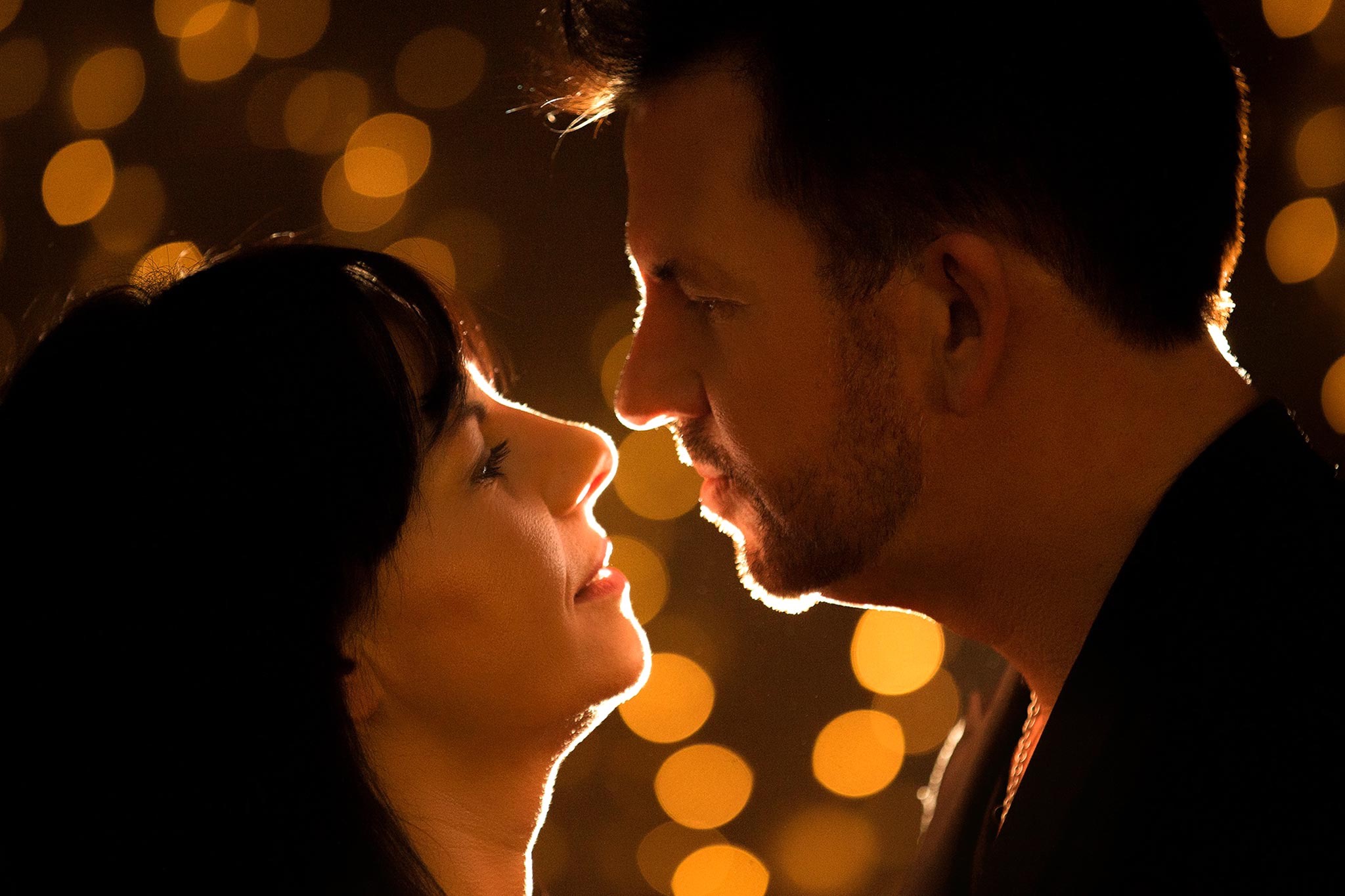 Profil kobiety i mężczyzny w zbliżeniu, oświetleni ciepłym światłem, z rozmytym tłem z bokeh