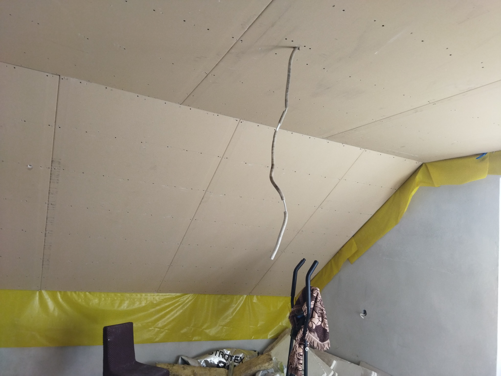 Poddasze z zamontowanymi płytami kartonowo-gipsowymi, widoczna instalacja elektryczna i folia ochronna, przygotowane do dalszych prac wykończeniowych.