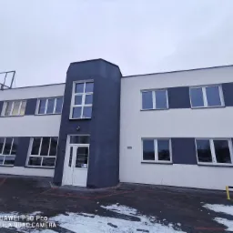 Dwukondygnacyjny budynek biurowy z szaro-białą fasadą, widoczne okna i wejście z białymi drzwiami, adres na ścianie: Ul. Rapackiego 65.