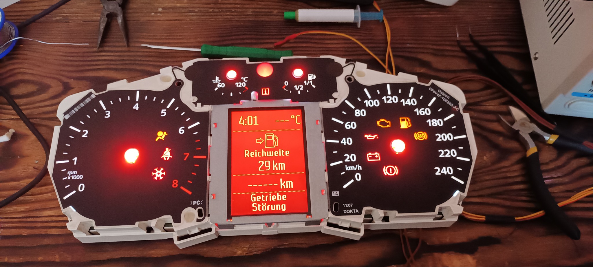 Demontaż deski rozdzielczej samochodu z widocznymi narzędziami i podświetlonymi ikonami diagnostycznymi, w tym ostrzeżenie o niskim zasięgu i usterce skrzyni biegów.