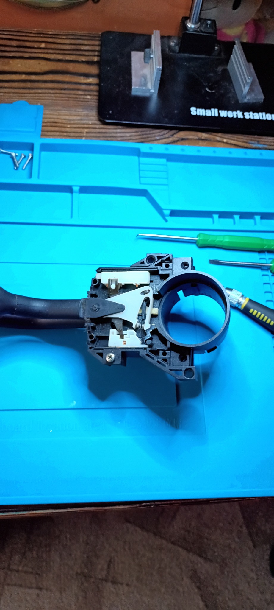 Demontaż przełącznika zespolonego świateł i kierunkowskazów na niebieskiej macie warsztatowej, widoczne śrubokręty i narzędzia.