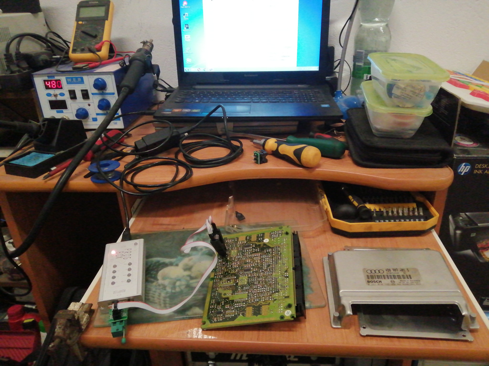 Stół warsztatowy z elektroniką samochodową: laptop, multimetr, stacja lutownicza, sterownik silnika Audi Bosch 4B0 907 401 S, programator Ruapier i narzędzia do diagnostyki.