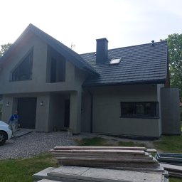 MAR-BUD Marcin Sokołowski - Dom jednorodzinny z szarą elewacją w trakcie prac wykończeniowych, widoczny pracownik w kombinezonie, stos desek i rusztowanie na pierwszym planie.