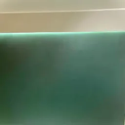 Świeżo pomalowana na zielono ściana z podświetleniem LED w górnej części, widoczny fragment sufitu i listwy przypodłogowej.