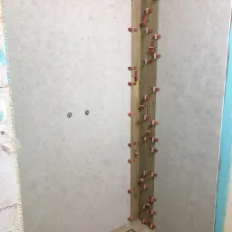 Montaż płytek imitujących drewno w narożniku łazienki, widoczne krzyżyki dystansowe, odpływ liniowy w podłodze, fragment ściany z szarą płytką.