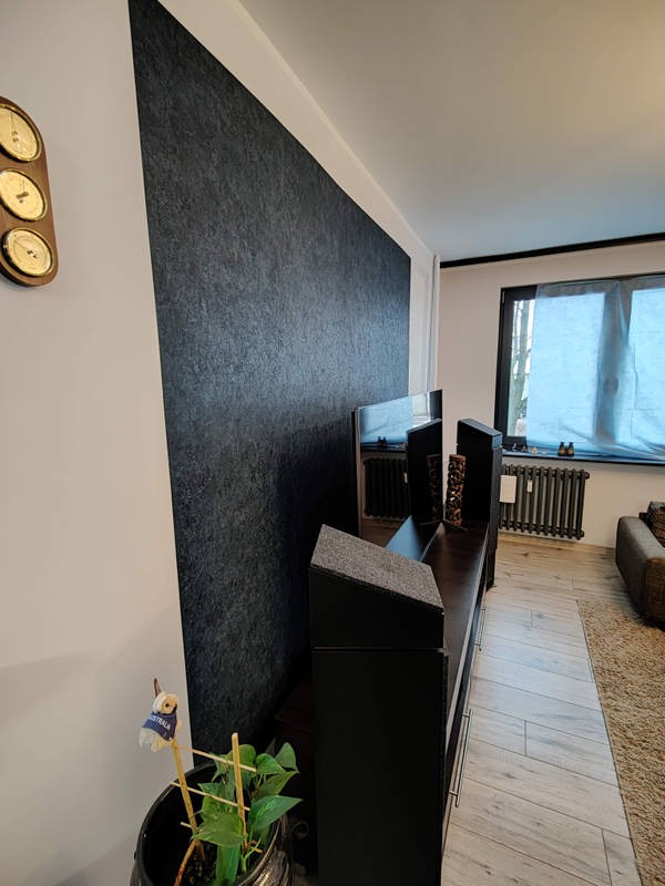 Nowoczesne wnętrze salonu z czarną ścianą akcentową, drewnianą podłogą ułożoną w jodełkę i czarnym grzejnikiem pod oknem.