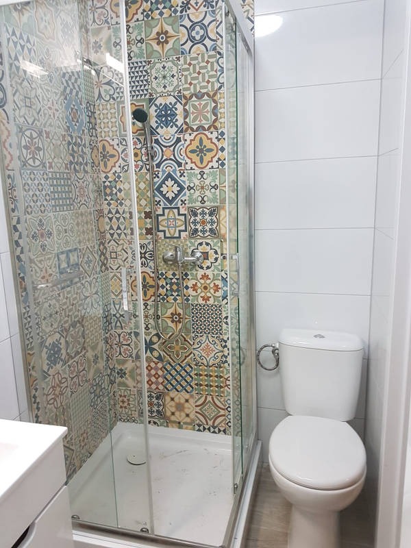 Nowoczesna kabina prysznicowa z wielobarwnymi, wzorzystymi płytkami na ścianie, widoczny biały sedes i umywalka, jasne wnętrze łazienki.