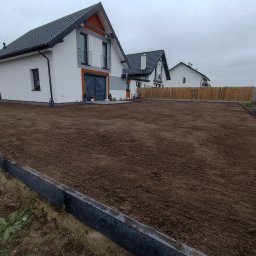 Art Bruk Joachim Jankowski - Przygotowany teren pod przyszły ogród z obrzeżami, w tle nowoczesne domy jednorodzinne i drewniane ogrodzenie.