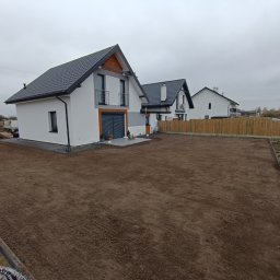 Art Bruk Joachim Jankowski - Przygotowany teren pod trawnik przed nowym domem z kostką brukową i drewnianym ogrodzeniem w tle.