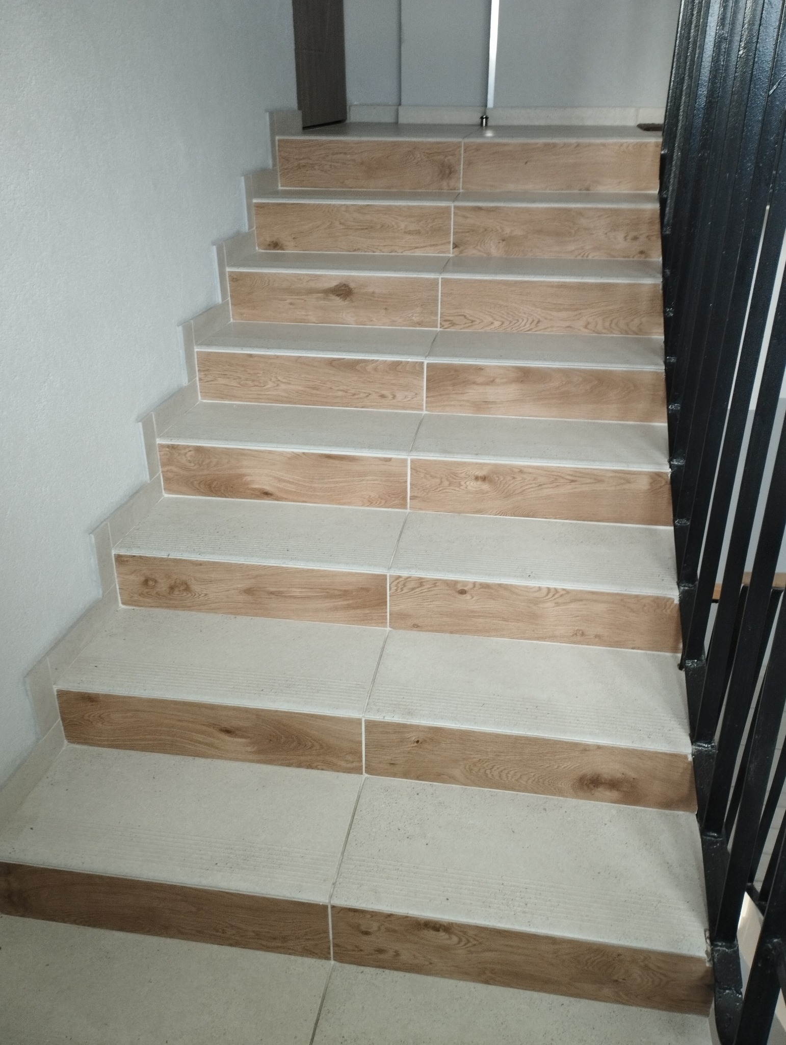 Schody wyłożone płytkami imitującymi drewno, z czarną metalową barierką, widok z dołu.