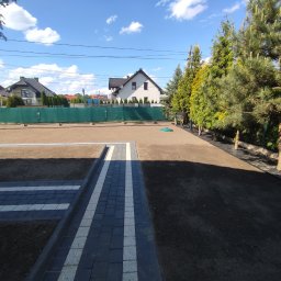 Usługi remontowo budowlane Krzysztof Kasprusz - Przygotowany teren pod trawnik z rolki, widoczny fragment ścieżki z kostki brukowej w kolorze szaro-białym, w tle ogrodzenie z siatki maskującej i zabudowa jednorodzinna.