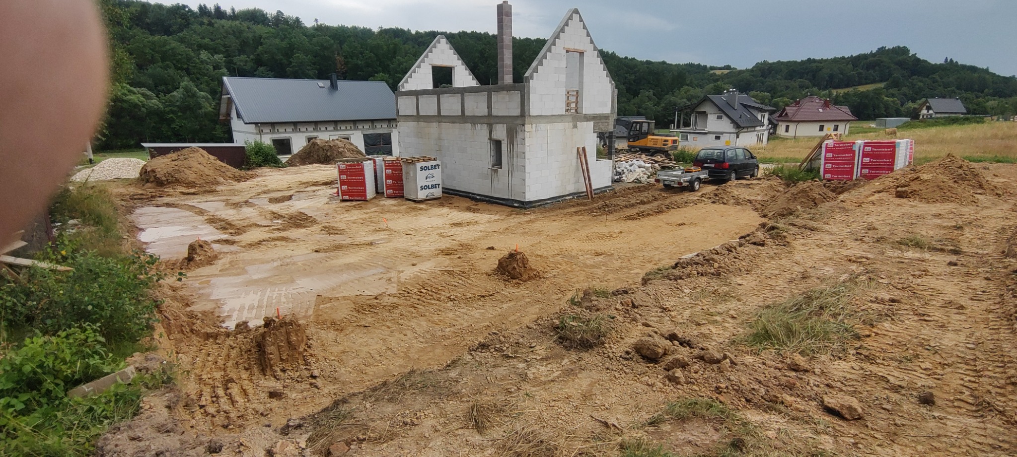 Budowa domu jednorodzinnego w trakcie realizacji: wzniesione ściany z betonu komórkowego, przygotowany teren, widoczny sprzęt budowlany i materiały budowlane Solbet i Termobet, krajobraz...