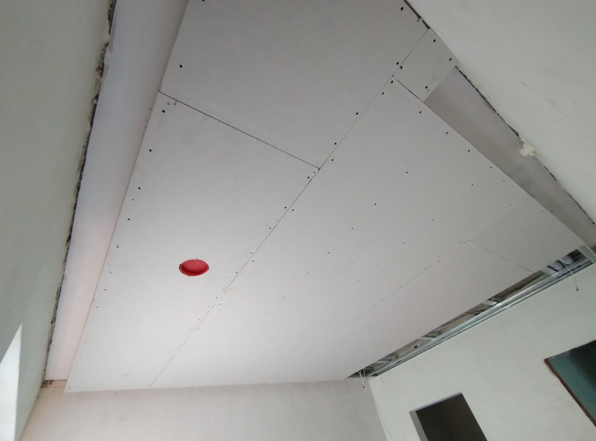 Montaż sufitu podwieszanego z płyt kartonowo-gipsowych, widoczne łączenia płyt i otwór pod oświetlenie.