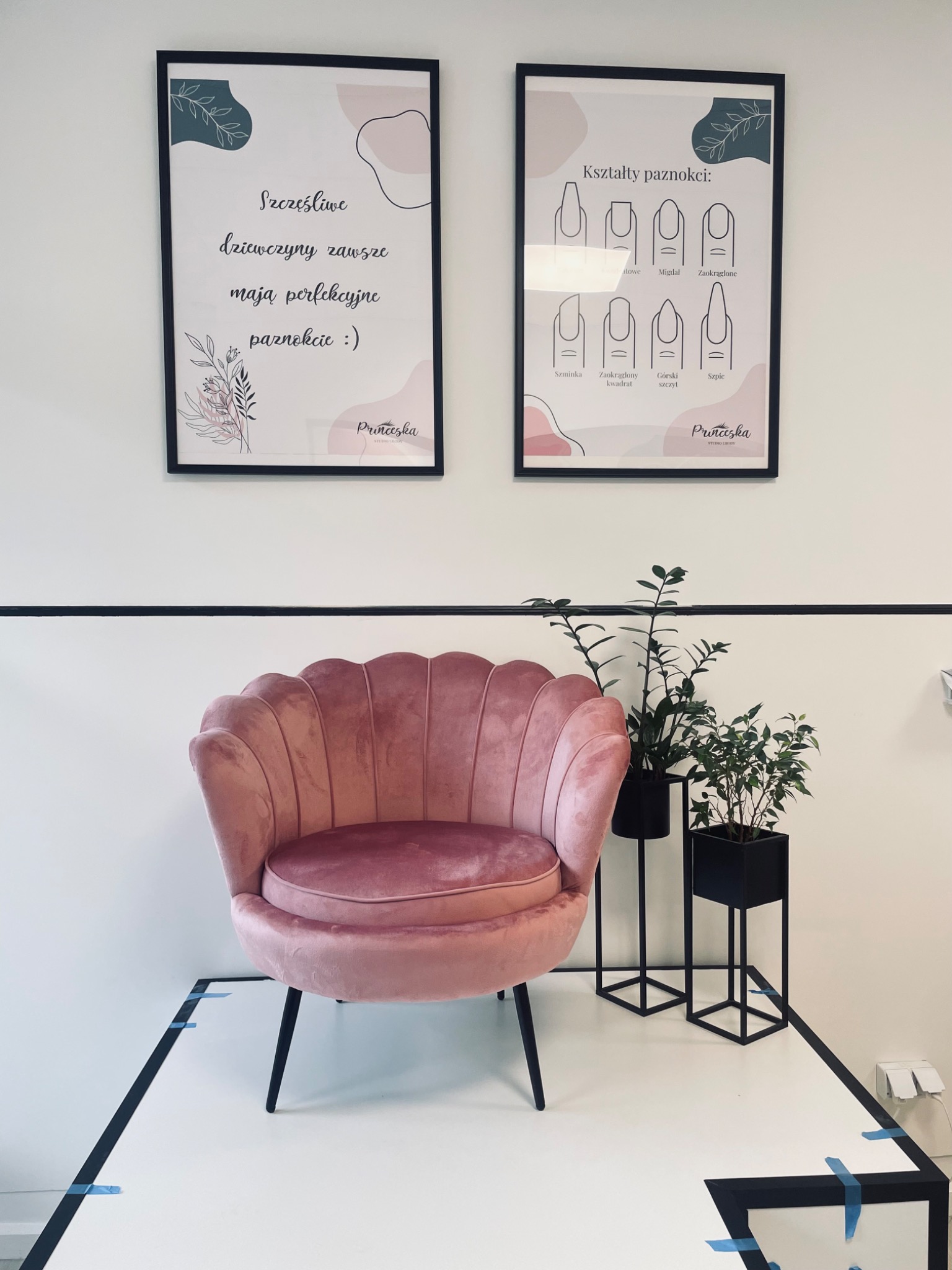 Różowy fotel muszelka w salonie kosmetycznym, plakaty z kształtami paznokci i hasłem 'Szczęśliwe dziewczyny...', rośliny w czarnych doniczkach.