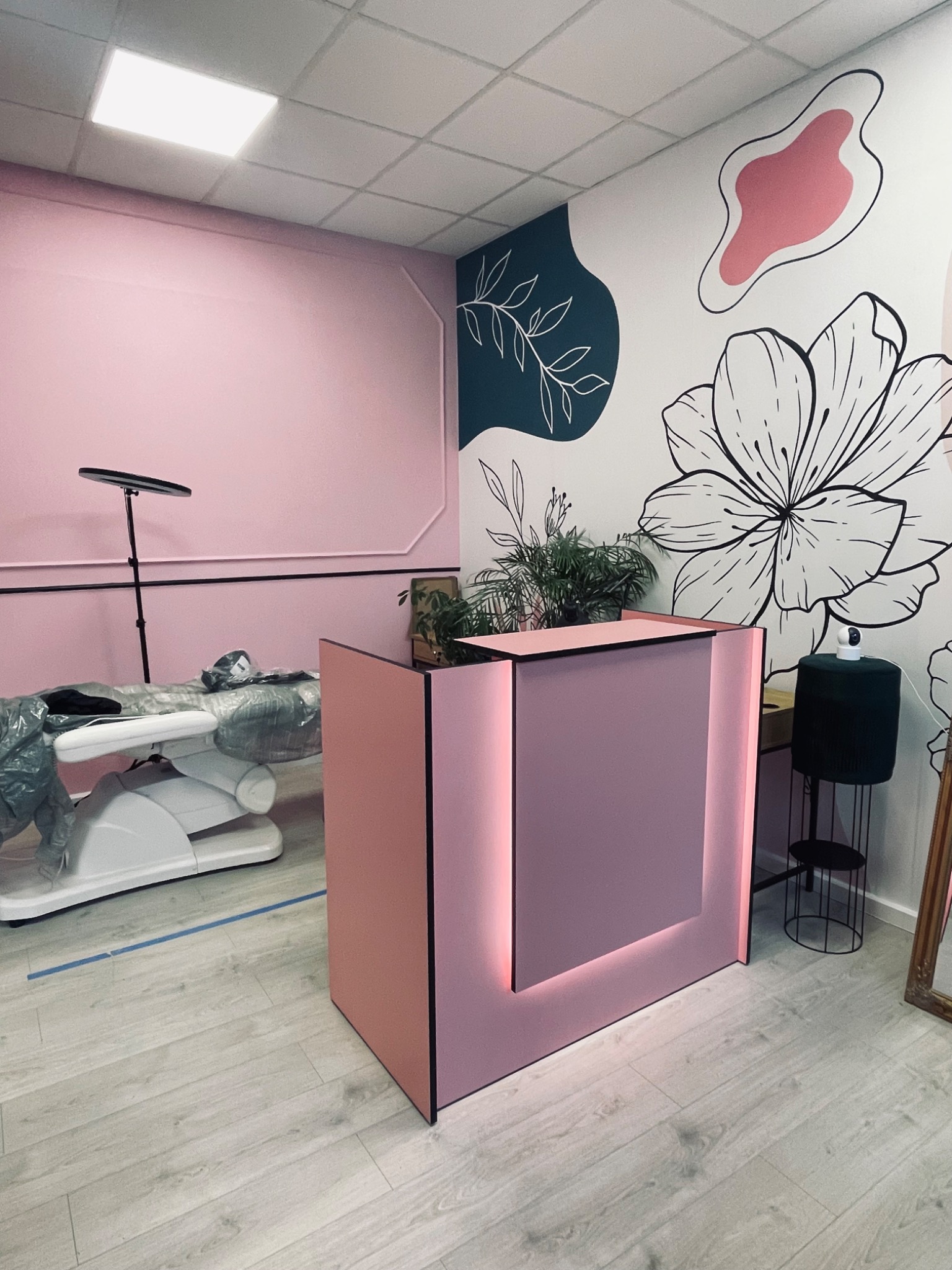 Różowe wnętrze salonu kosmetycznego z recepcją i fotelem zabiegowym, ozdobione minimalistycznymi malunkami kwiatów na ścianie. Nowoczesny design.