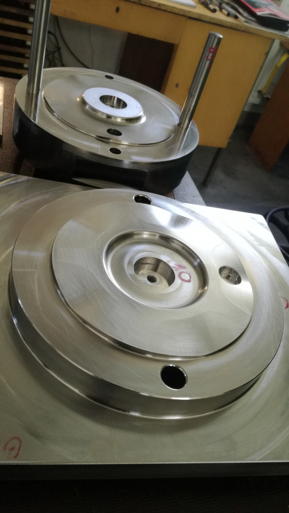 Dwa elementy tłocznika z obrobionego metalu. Na górnym elemencie widoczne dwa trzpienie, a na dolnym czerwone oznaczenia. Obróbka powierzchni widoczna.