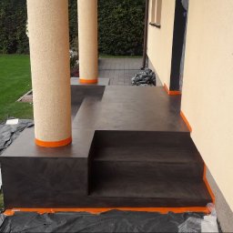 Liubomyr Ovchar - Zewnętrzne schody wejściowe i taras wykończone ciemnym, polerowanym materiałem z pomarańczowymi akcentami, widoczne kolumny z fakturą i zabezpieczenia folią malarską.