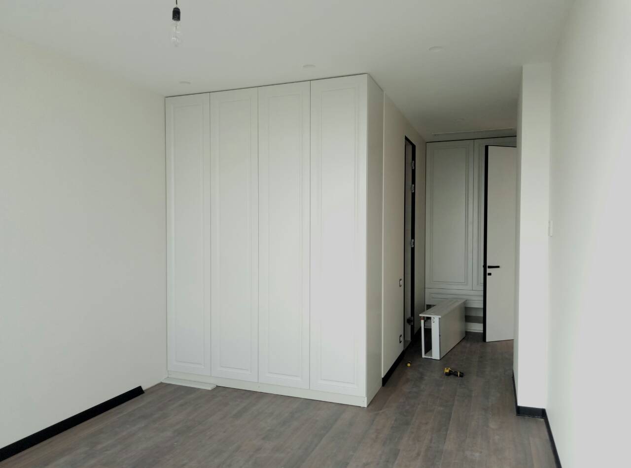 Wnętrze pokoju z zamontowaną białą szafą w zabudowie, szarą podłogą imitującą drewno i widocznymi narzędziami montażowymi na podłodze.