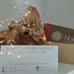 Karta podarunkowa na masaż lub zabiegi medycyny naturalnej w studio Holistic w Zamościu, obok róża pustyni i dekoracyjne lampki.